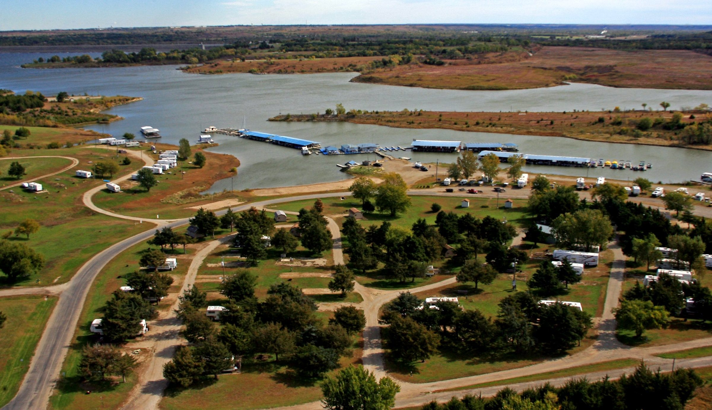 Aerial view of the resort: winding roads through tree-shaded RV sites with the marina docks and Milford Lake beyond