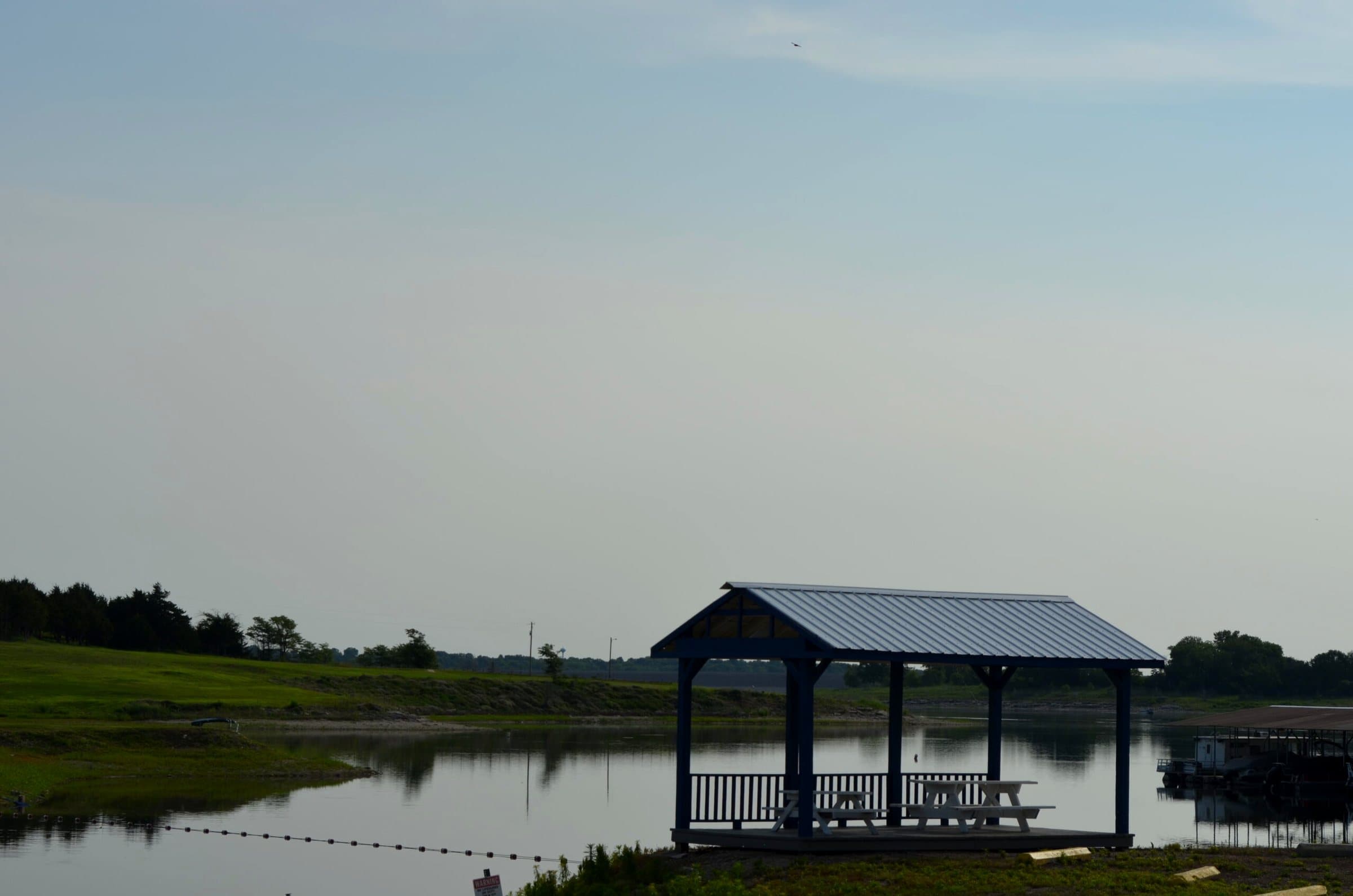 Gazebo with a metal roof on the shore, calm water in front