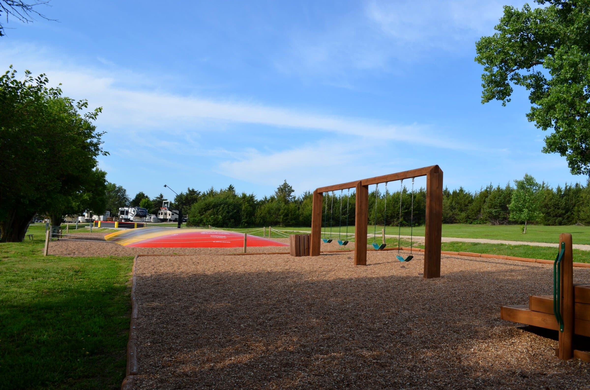 Red jumping pillow beyond a wooden swing set on a wood-chip path